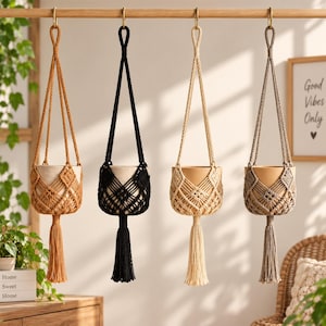 May include: Four macrame plant hangers suspended from a wooden rod, each featuring a knotted cord design and a long tassel at the bottom. The hangers are in mustard yellow, black, cream, and taupe, each holding a plain, neutral-colored plant pot.