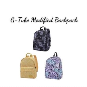 May include: Three backpacks labeled G-Tube Modified Backpack. One is black with a white tie-dye pattern, one is solid gold, and one features a purple and blue leopard print. Each bag has a top handle, shoulder straps, and a front zippered pocket.