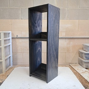 May include: A black wooden shelf unit with two shelves. The shelves are open and the unit is made of wood with a dark stain.