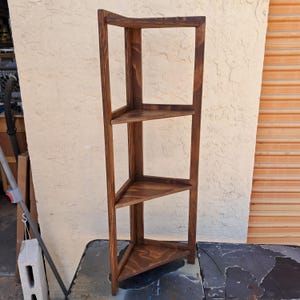 May include: A wooden corner shelf with three triangular shelves. The shelves are stained a dark brown color and are supported by a frame. The shelf is designed to fit into a corner and maximize space.