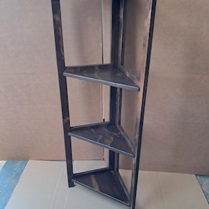 May include: A dark stained wooden corner shelf with three triangular shelves. The shelves are supported by a dark frame. The shelf is designed to fit into a corner and is made of wood.