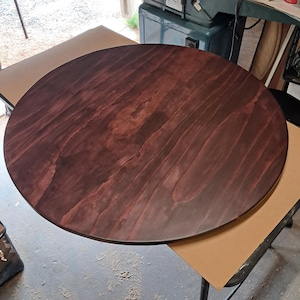 May include: A large, round wooden tabletop with a rich, dark reddish-brown stain. The wood grain is visible, creating a natural pattern. The tabletop is unfinished and ready for use. The diameter is approximately 30 inches.