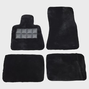 May include: A set of four black plush car floor mats. The set includes two rectangular mats, one larger contoured mat, and one smaller mat featuring a rectangular black heel pad with a grid pattern stitched into the center surface.