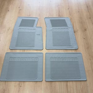 Könnte beinhalten: Ein Set aus vier hellgrauen Automatten. Die beiden vorderen Matten haben eine asymmetrische Form mit einer rechteckigen, strukturierten Fersenauflage und einem gerippten Bereich, während die beiden hinteren Matten rechteckig sind.