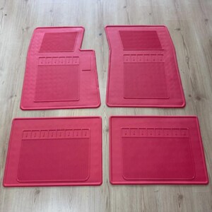Pode incluir: Um conjunto de quatro tapetes de borracha para automóvel em vermelho vivo. Os dois tapetes dianteiros apresentam um design com um canto recortado, enquanto os dois traseiros são retangulares. Cada tapete tem um padrão de grelha texturizado.