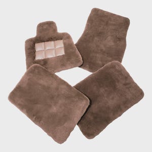 May include: A set of four brown faux fur car floor mats. Three mats are rectangular with rounded corners, while one mat features a distinct notched top edge with a central rectangular panel containing a grid of six padded squares.