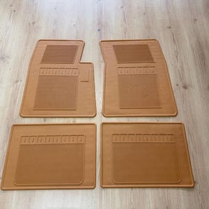 Op de afbeelding: Een set van vier bruine automatten met een gestructureerd rechthoekig grip-patroon in het midden en een kleiner rechthoekig gedeelte aan de bovenkant. De twee voorste matten hebben een asymmetrische vorm, terwijl de achterste matten rechthoekig zijn.