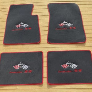Könnte beinhalten: Ein Set aus vier schwarzen Automatten mit roter Umrandung an den Kanten. Jede Matte zeigt ein gesticktes Logo mit einer rot-weißen Zielflagge, der Silhouette eines springenden Hirsches und dem roten Schriftzug Impala SS in der Mitte.