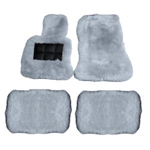 May include: A set of four light gray faux fur car floor mats. The set includes two rectangular rear mats and two front mats, with one front mat featuring a black rectangular insert with a grid pattern. The mats have a thick, shaggy texture.