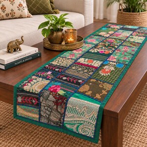 Peut inclure: Un chemin de table rectangulaire composé d'un assemblage de carrés de tissu verts, roses et dorés. Le chemin présente des broderies complexes, des motifs floraux et des accents de fils métalliques, avec une bordure verte unie.