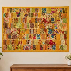 May include: A rectangular wall hanging featuring a patchwork design of various fabric strips in shades of yellow, orange, red, green, and blue. The textile displays intricate embroidery, floral patterns, and metallic accents, all bordered by a solid yellow frame.