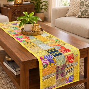 Peut inclure: Un chemin de table rectangulaire présentant un motif patchwork composé de divers carrés de tissu aux couleurs vives, notamment jaune, rose, bleu et vert. Le chemin est orné de broderies complexes, de perles et de paillettes, avec une bordure jaune unie.