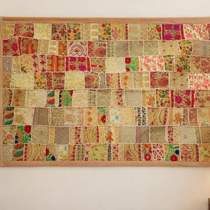 May include: A rectangular wall hanging featuring a patchwork design of various fabric squares in shades of gold, beige, and cream, accented with vibrant floral patterns in red, pink, green, and blue, suspended from a wooden rod at the top.