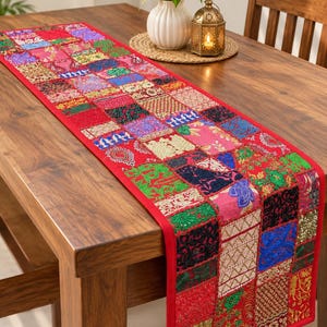 Könnte beinhalten: Ein rechteckiger Tischläufer mit einem lebendigen Patchwork-Design, das aus zahlreichen kleinen, bunten Stoffquadraten besteht. Der Läufer zeigt eine Vielzahl komplizierter Muster, Texturen und Stickereien in Rot-, Grün-, Blau- und Goldtönen.