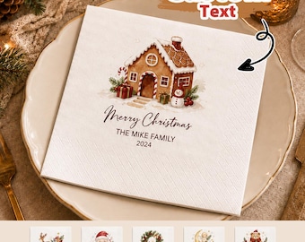Könnte beinhalten: Eine quadratische weiße Papierserviette mit einer Aquarellillustration eines Lebkuchenhauses, eines Schneemanns und Geschenken. Der Text lautet Merry Christmas, THE MIKE FAMILY und 2024. Die Serviette hat eine strukturierte Oberfläche.
