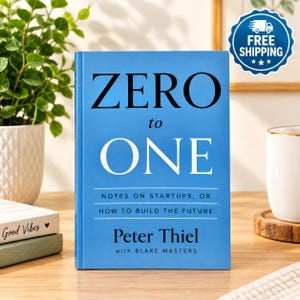 May include: A blue hardback book titled Zero to One: Notes on Startups, or How to Build the Future by Peter Thiel with Blake Masters. The front cover features bold black and white text centred on a solid blue background, standing upright.