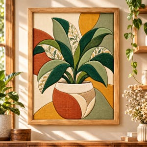 May include: A framed textile wall art piece featuring a stylized potted plant with layered fabric leaves in shades of dark green, light green, and cream with a leaf pattern. The pot is rounded with orange, cream, and tan fabric segments.