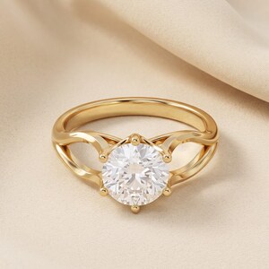 Peut inclure: Une bague en or avec une pierre précieuse ronde, transparente et facettée, maintenue par un sertissage à six griffes. L'anneau présente un design divisé qui se courbe vers le haut pour rejoindre la pierre centrale, avec une finition polie.