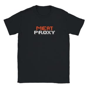 Puede incluir: Una camiseta negra de manga corta con el texto MEAT PROXY impreso en una fuente pixelada. La palabra MEAT es de color naranja y la palabra PROXY es de color blanco. La camiseta tiene cuello redondo y corte estándar sobre fondo liso.