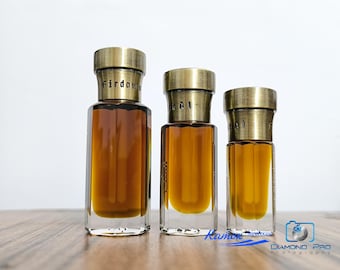 Può includere: Tre flaconi di profumo in vetro trasparente di diverse altezze riempiti con liquido color ambra. Ogni flacone presenta una base esagonale e un tappo metallico color ottone antico. Il flacone più grande riporta la scritta Firdaws.