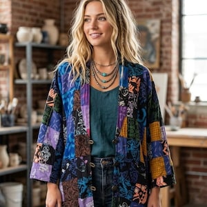 May include: A long-sleeved, open-front jacket featuring a patchwork design with various blue, purple, black, and orange patterned fabric squares. The garment is worn over a solid dark teal top and dark blue denim jeans, paired with a multi-strand necklace.
