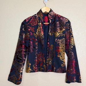 May include: A long-sleeved jacket in a dark navy blue base color featuring a vibrant, multi-colored floral and scroll pattern in shades of red, orange, and gold. The jacket has a high collar, a front button closure, and slightly flared sleeves.