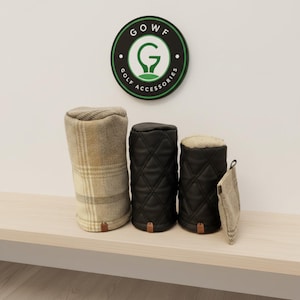 Könnte beinhalten: Ein Set aus drei Golfschlägerhauben und einem kleinen quadratischen Beutel. Eine Haube besteht aus beigegrauem Karostoff, während zwei Hauben aus schwarzem Steppmaterial gefertigt sind. Jeder Artikel hat eine kleine braune Lederlasche. Ein rundes Schild zeigt die Aufschrift GOWF GOLF ACCESSORIES.