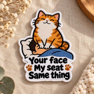 May include: An embroidered patch featuring an orange tabby cat sitting on a person's face while they sleep under a blue blanket. The patch includes the black text: Your face My seat Same thing, with two small orange paw prints on the sides.