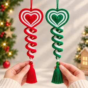 May include: Two crocheted hanging ornaments, one red and white and one green and white. Each features a heart-shaped top with concentric stripes, a spiraling tail, a small white bead, a faceted colored bead, and a matching yarn tassel at the base.