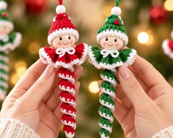 Peut inclure: Deux décorations en crochet en forme de personnages avec des visages ronds, portant des bonnets pointus et des cols à volants. Un personnage est rouge et blanc, l'autre est vert et blanc. Ils ont des corps en spirale et des cordons.