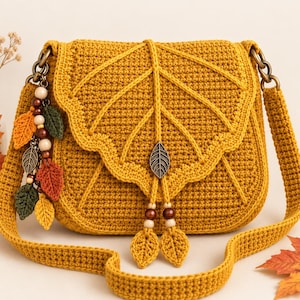 Puede incluir: Un bolso de hombro de ganchillo color amarillo mostaza con una solapa en forma de hoja grande con costuras en relieve. El bolso incluye una correa a juego, un dije de hoja de metal y una borla lateral de hojas pequeñas y cuentas de madera.