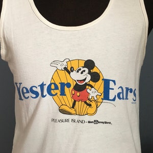 May include: White tank top with a blue and yellow graphic of Mickey Mouse on Pleasure Island at Walt Disney World. The text "Yester Ears" is printed in blue.