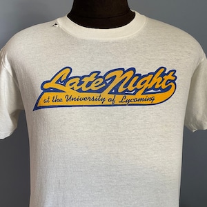 May include: White t-shirt with a blue and yellow graphic that says "Late Night at the University of Lycoming".