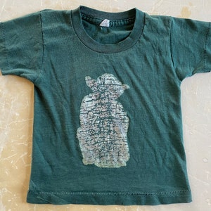 May include: A dark green t-shirt with a silver-colored Yoda silhouette graphic print.