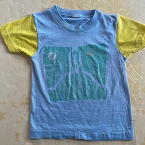 May include: A blue and yellow short-sleeved t-shirt with a green and blue graphic design. The graphic design features a geometric shape with the text "Universal" in a small font.