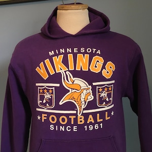 May include: Purple hooded sweatshirt with the Minnesota Vikings logo and the text "Minnesota Vikings Football Since 1961".