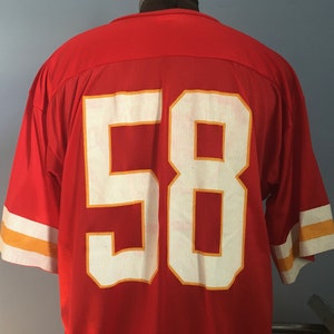 May include: Red football jersey with white number 58 outlined in gold. The jersey has white and gold stripes on the sleeves.