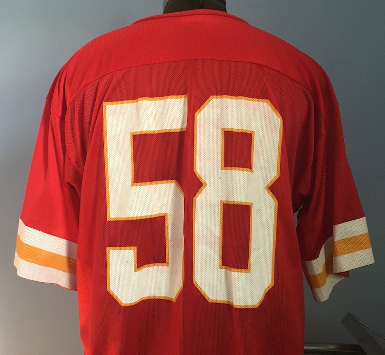 May include: Red football jersey with white number 58 outlined in gold. The jersey has white and gold stripes on the sleeves.