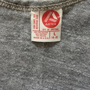 May include: A gray tag with white text that reads "FOR CARE, SEE REVERSE SIDE ARTEX DIV. OF JOSTENS 50% POLYESTER 40% COTTON 10% RAYON MADE IN USA. L 14-16"