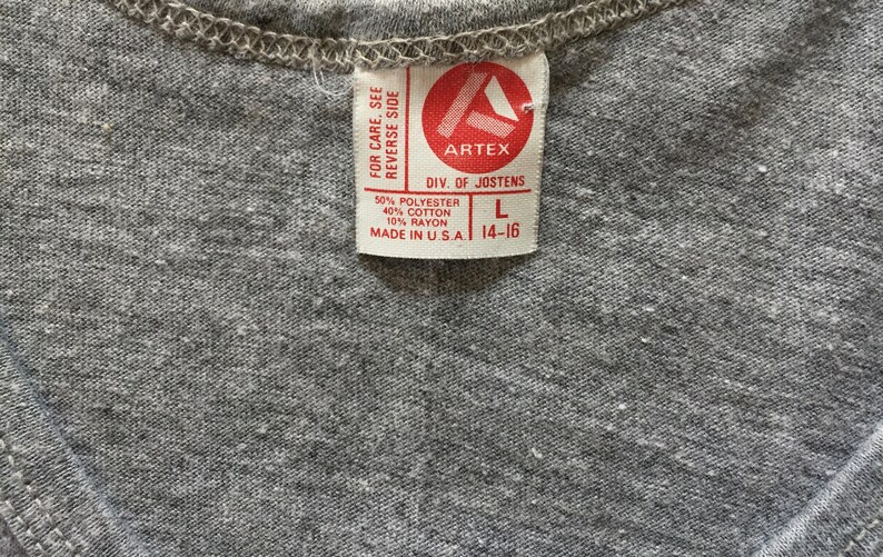 May include: A gray tag with white text that reads "FOR CARE, SEE REVERSE SIDE ARTEX DIV. OF JOSTENS 50% POLYESTER 40% COTTON 10% RAYON MADE IN USA. L 14-16"