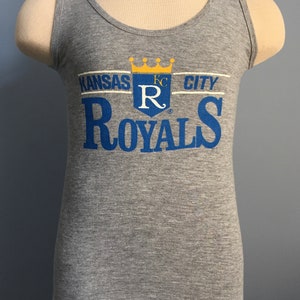 May include: Gray tank top with a blue and yellow Kansas City Royals logo. The logo features a crown, the letters "KC" and a large "R" with a stylized "ROYALS" below.