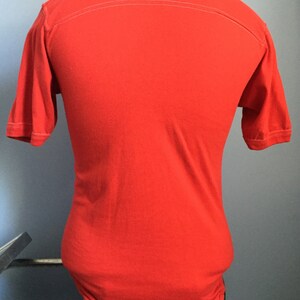 May include: A solid red short-sleeved t-shirt with a white seam down the back.