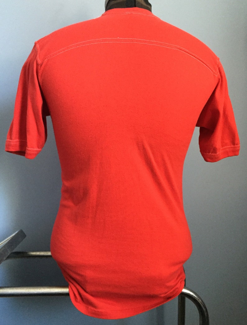 May include: A solid red short-sleeved t-shirt with a white seam down the back.