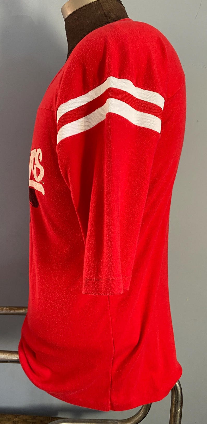 May include: Red long-sleeve shirt with white stripes on the sleeves. The shirt has a logo on the front. The shirt is displayed on a mannequin.