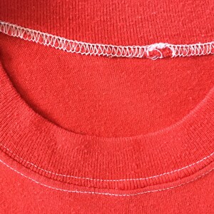 May include: Close-up of the neckline of a red t-shirt with white stitching.