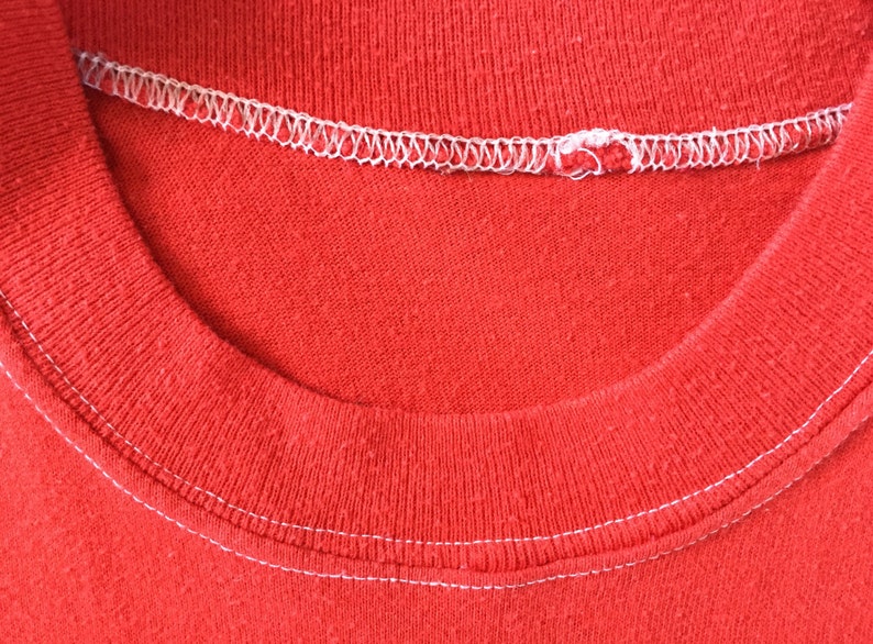 May include: Close-up of the neckline of a red t-shirt with white stitching.