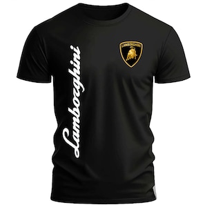 May include: A black short-sleeved t-shirt featuring the word Lamborghini written vertically in white script on the left side and the gold and black Lamborghini bull logo shield printed on the upper right chest area of the garment.