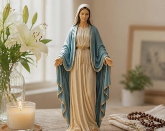 Può includere: Una statuetta in piedi della Vergine Maria che indossa una veste color crema e un mantello azzurro con bordi dorati. La figura ha un velo sul capo, le mani tese verso l'esterno e poggia su una base circolare.