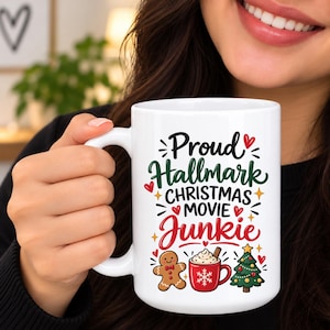 May include: A white ceramic mug featuring the black, green, and red text Proud Hallmark CHRISTMAS MOVIE Junkie. The design includes small red hearts, yellow stars, a brown gingerbread man, a red mug with whipped cream, and a green Christmas tree.