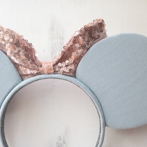 Pu&ograve; includere: Orecchie di topo blu chiaro con un fiocco di paillettes oro rosa.